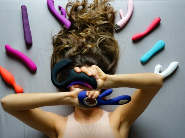 Woman Lying on the Floor and Holding a Variety of Different Vibrators